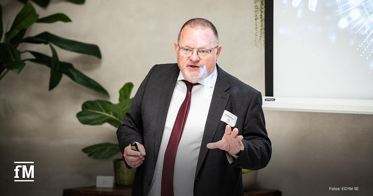 Ein Mann im Anzug spricht während einer Präsentation, im Hintergrund eine Leinwand