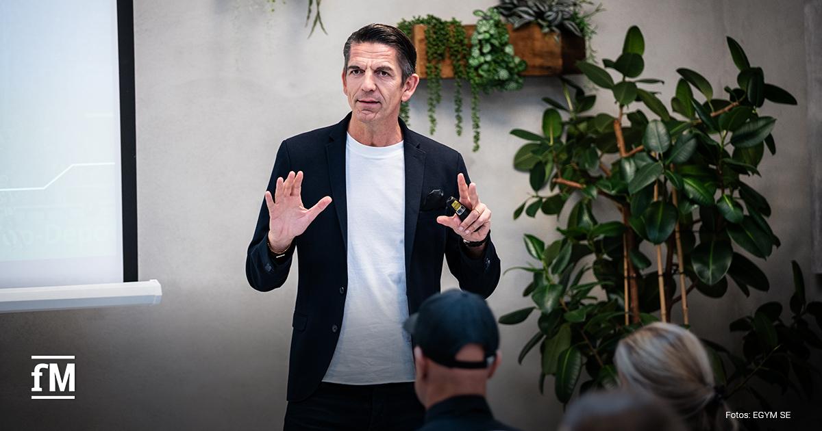 Ein Mann im Sakko spricht während einer Präsentation vor Publikum, Pflanzen im Hintergrund