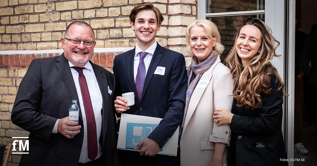 Vier Personen in Businesskleidung stehen nebeneinander und lächeln in die Kamera