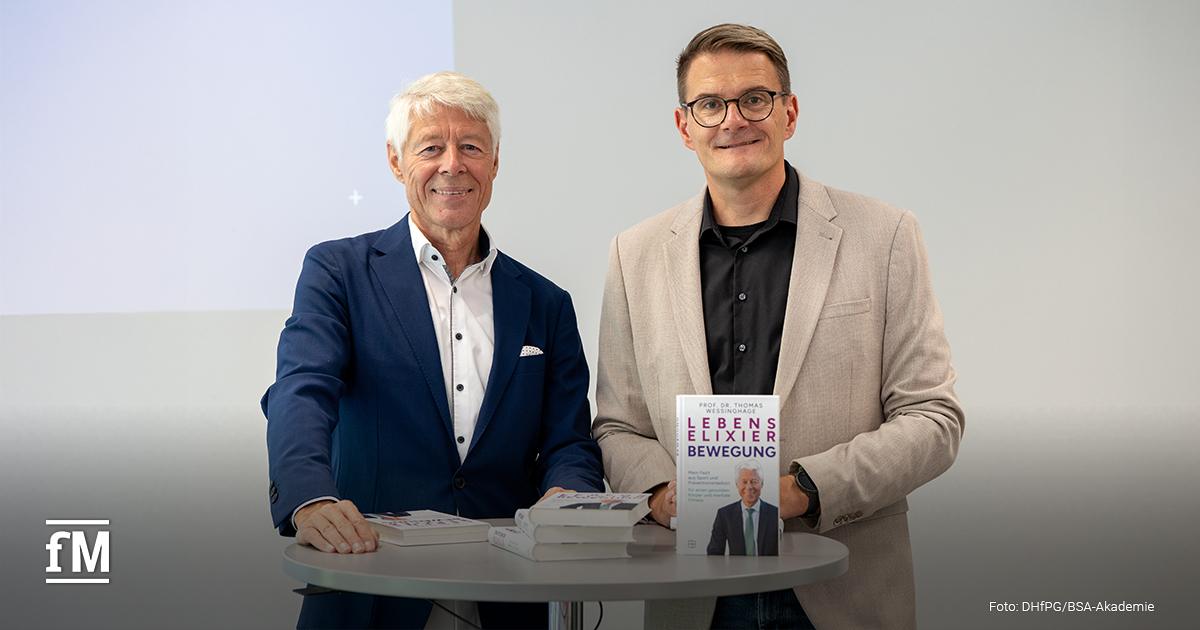 Zwei Männer stehen nebeneinander an einem Stehtisch. Links Prof. Dr. Thomas Wessinghage im blauen Anzug, rechts ein Moderator im beigen Sakko. Beide halten das Buch 'Lebenselixier Bewegung' in der Hand.