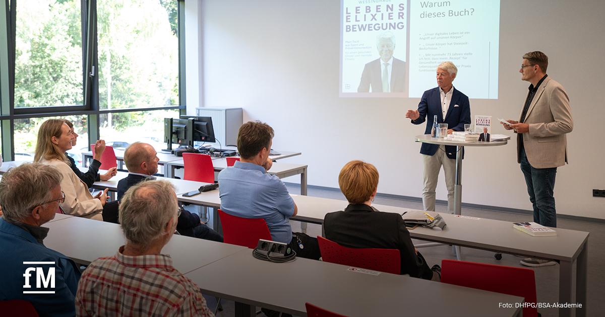 Prof. Dr. Thomas Wessinghage und ein Moderator sprechen vor einem sitzenden Publikum. Hinter ihnen wird eine Präsentationsfolie mit dem Buchtitel 'Lebenselixier Bewegung' eingeblendet.