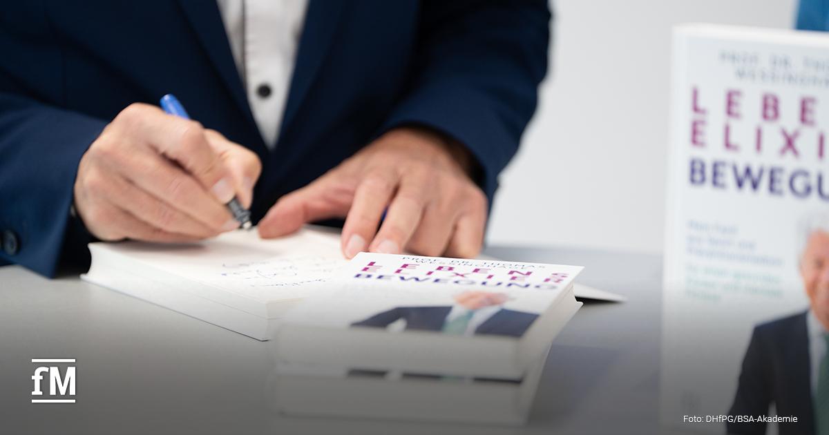 Nahaufnahme einer Hand, die mit einem Stift in ein Exemplar des Buches 'Lebenselixier Bewegung' schreibt.