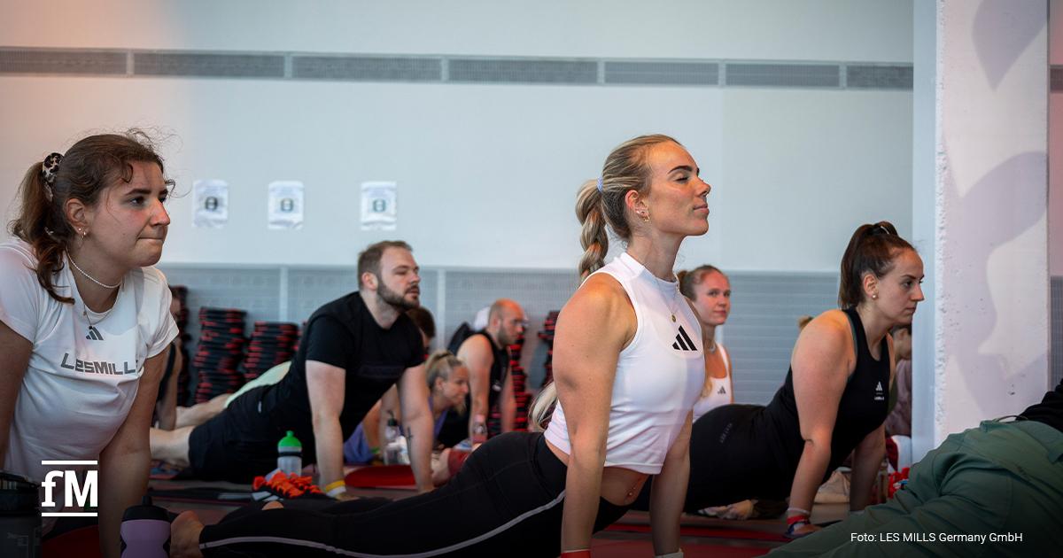 Gruppe führt Kobra-Pose aus, Frau im weißen Top im Vordergrund