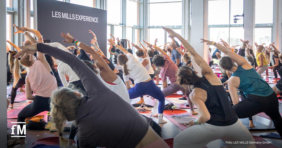 Gruppe macht seitliche Dehnübung vor Bühne mit Schriftzug „LES MILLS EXPERIENCE“