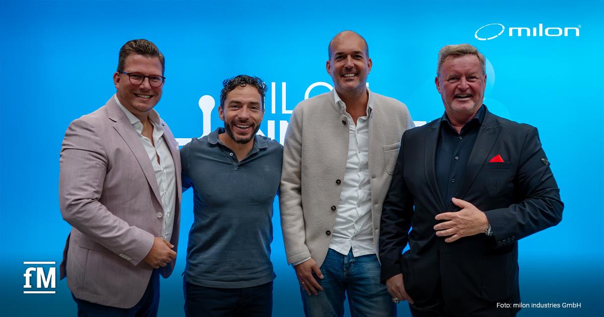 Vier Jury-Mitglieder des milon Innovation Hub Bootcamp stehen nebeneinander vor blauem Hintergrund. Alle tragen Business-Kleidung und lächeln in die Kamera.