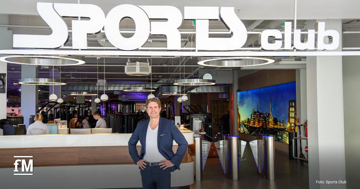 Sports Club-Inhaber Alexander Sosa steht im Anzug vor dem Eingang eines modernen Sports Club Studios.