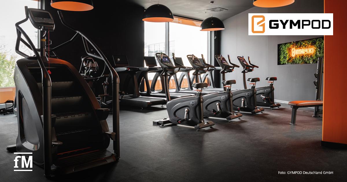 Innenansicht eines modernen Fitnessstudios mit Laufbändern, Fahrradergometern, Treppensteiger und Sitzbank; an der Wand ein Monitor mit GYMPOD-Logo.