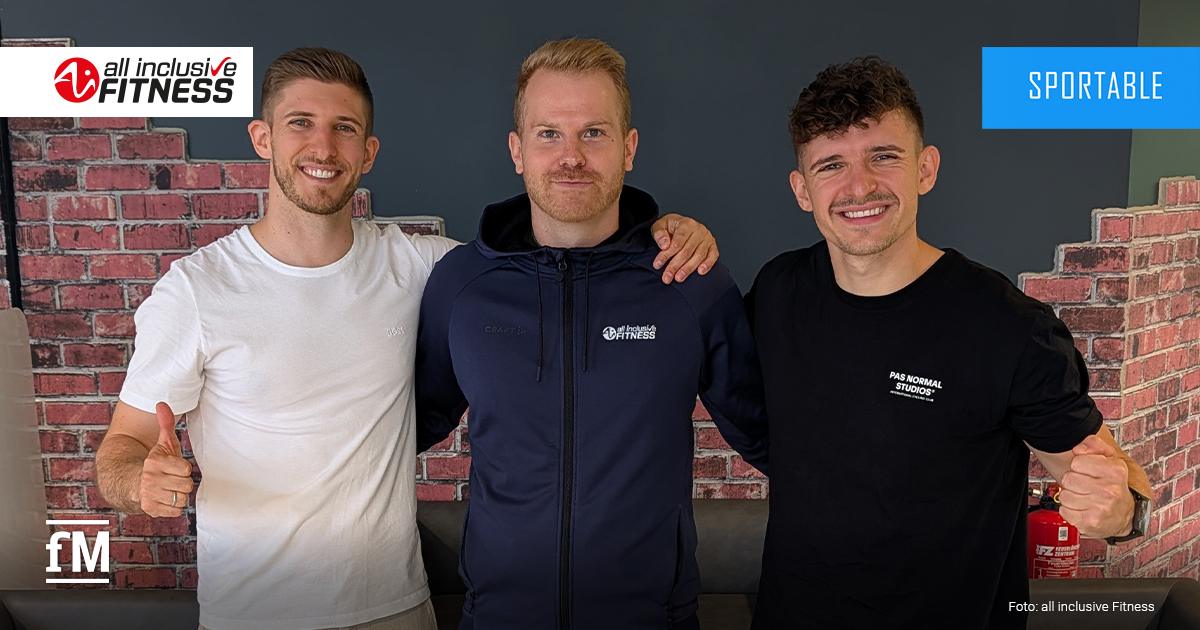 Drei junge Männer (Patrick Elbl, Nico Miller, Dominik Elbl) stehen lächelnd nebeneinander in einem Fitnessstudio vor einer Wand mit dem Logo 'all inclusive Fitness'.