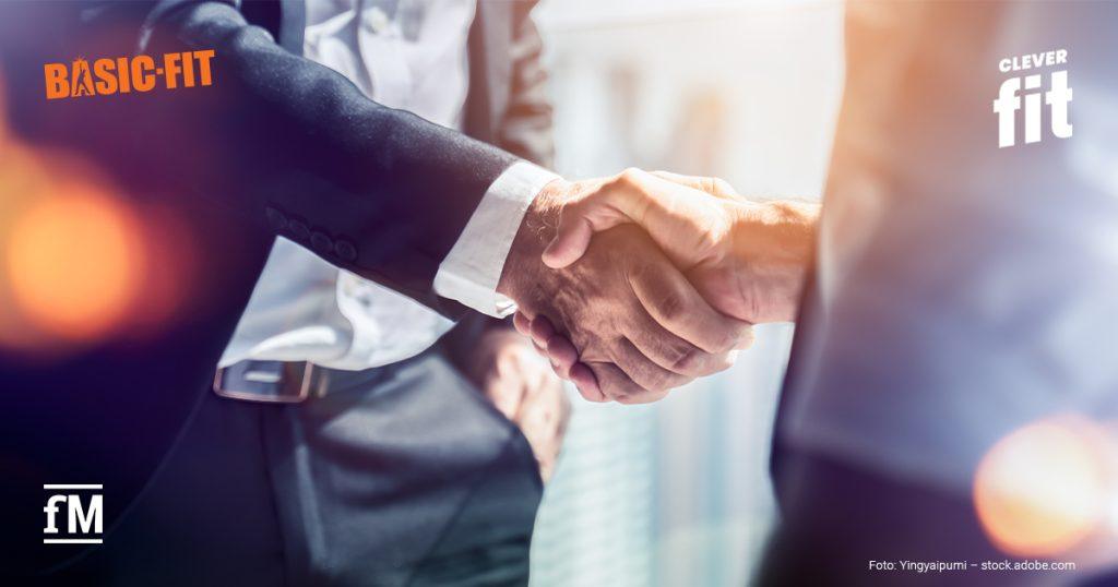 In einem modernen Bürogebäude geben sich zwei Geschäftspersonen in Anzügen die Hand.