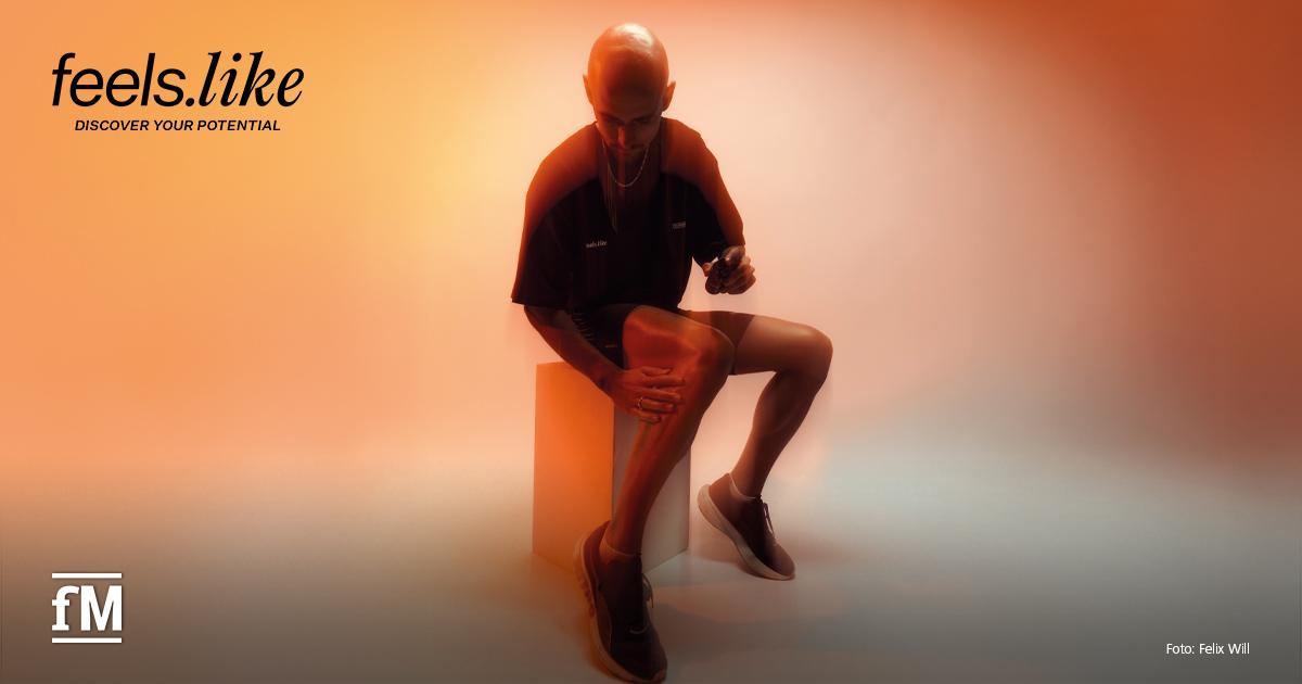 Eine Person sitzt auf einem Block in einem orange beleuchteten Raum und berührt ihr Knie. Links oben befindet sich das 'feels.like' Logo.