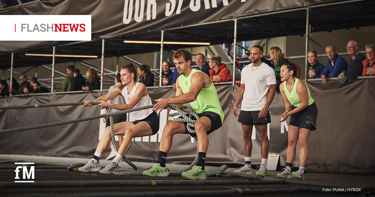 Bei einem HYROX-Fitnesswettkampf ziehen vier Personen gemeinsam an einem dicken Seil, während Zuschauer hinter einer Absperrung zuschauen.