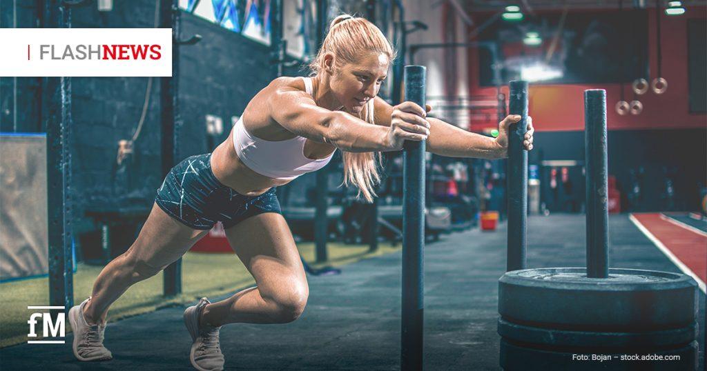 Eine Frau schiebt in einem Fitnessstudio ein mit Gewichten beladenes Trainingsschlittengerät und trainiert für ein HYROX-Event.