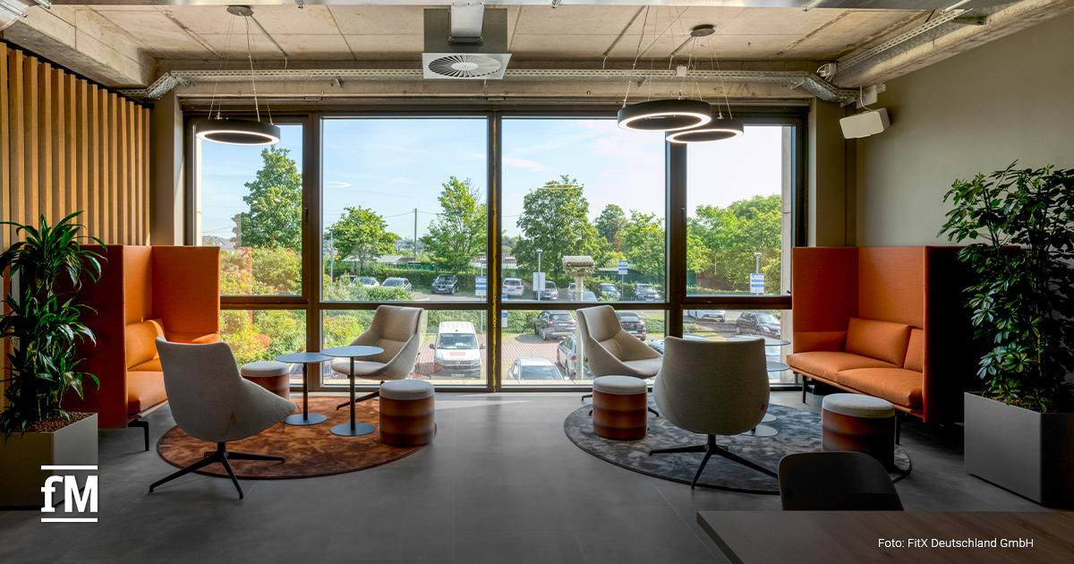 Loungebereich mit Sesseln, Sofas, runden Tischen und großen Fenstern mit Blick auf Bäume