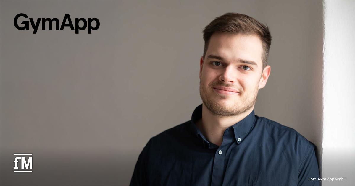Porträt eines Mannes im dunklen Hemd (Robin Lausch), der an einer weißen Wand steht; links oben steht das Logo 'GymApp'.