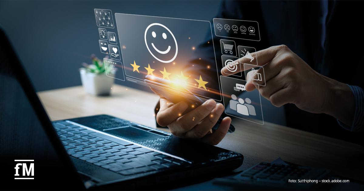 Eine Person nutzt Smartphone und Laptop, während digitale Symbole wie ein Smiley mit fünf Sternen, Einkaufswagen und Chat-Icons holografisch über dem Gerät erscheinen – Symbol für Kundenzufriedenheit und digitales Feedback.