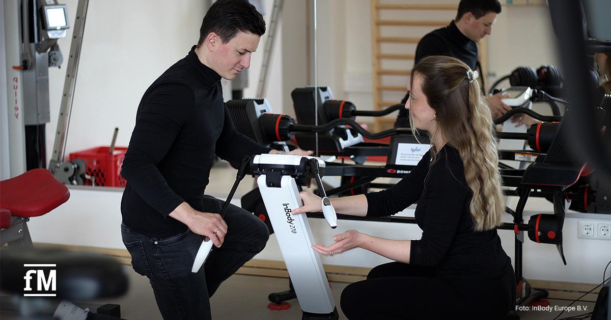 Zwei Personen knien vor einem InBody-Gerät und bereiten eine Messung in einem Fitnessraum vor.