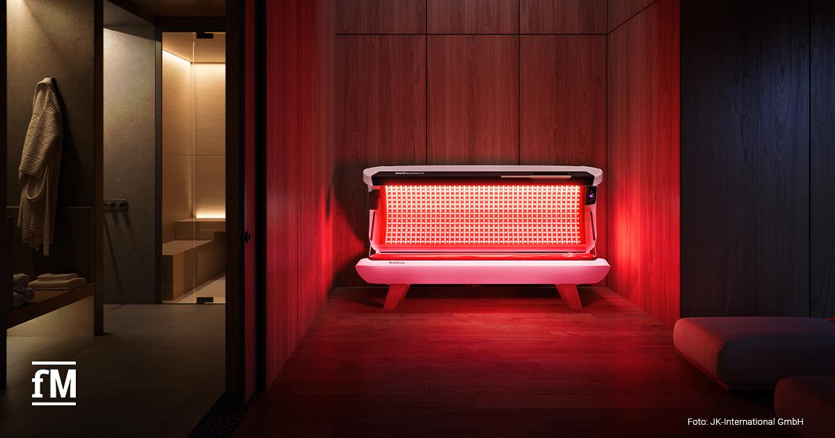Ein modernes Spa mit Holzverkleidung und gedämpfter Beleuchtung. In der Mitte steht ein wellsystem Redlight-Gerät, das in warmem Rotlicht leuchtet.