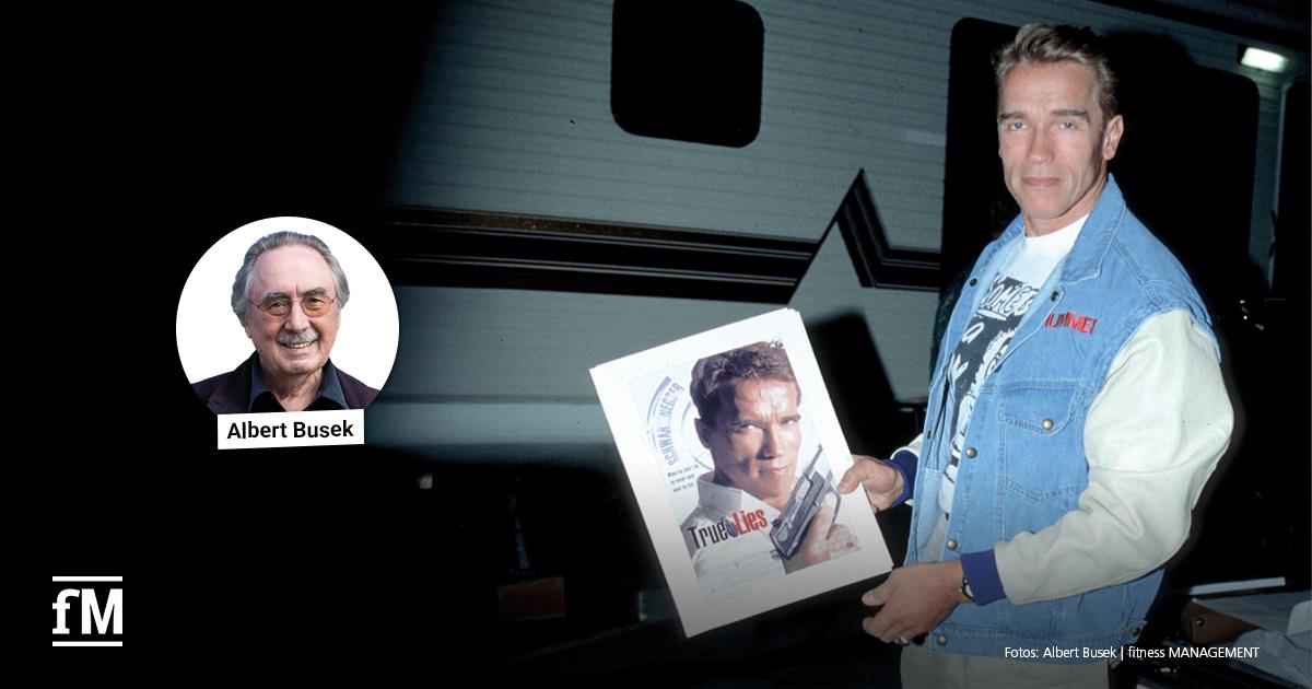 Sein und Schein beim Körpertraining Arnold Schwarzenegger hält ein Filmplakat zu 'True Lies'; links im Bild ein Porträtfoto von Albert Busek mit Namensbeschriftung.