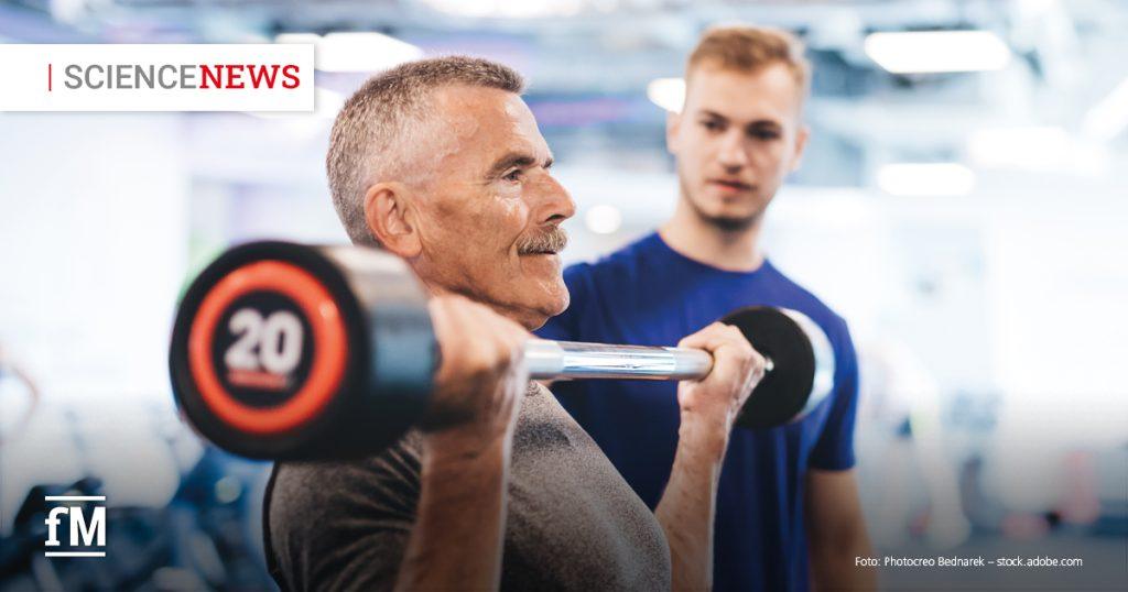 Älterer Mann hebt eine Hantel im Fitnessstudio, während ein Trainer ihn beobachtet.