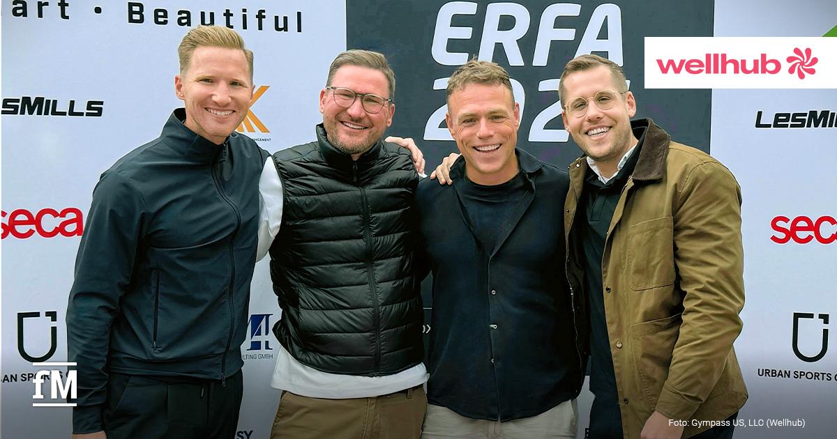 Bei einem Event stehen vier Männer gemeinsam lächelnd vor einer Sponsorenwand.