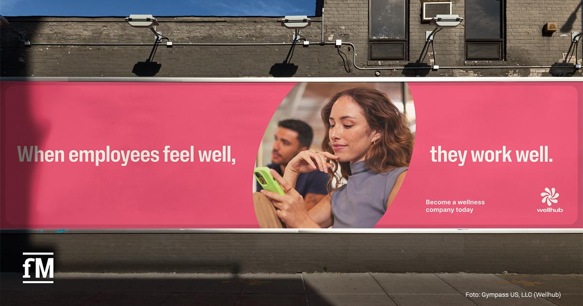 Großes Werbeplakat von Wellhub mit pinkem Hintergrund und dem Slogan 'When employees feel well, they work well'.