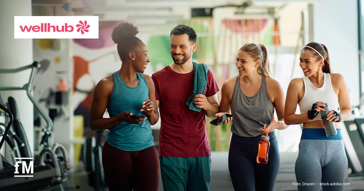 Wellhub State of Work-Life Wellness Report 2026 Vier Personen in Sportkleidung gehen lachend durch ein Fitnessstudio und unterhalten sich miteinander.