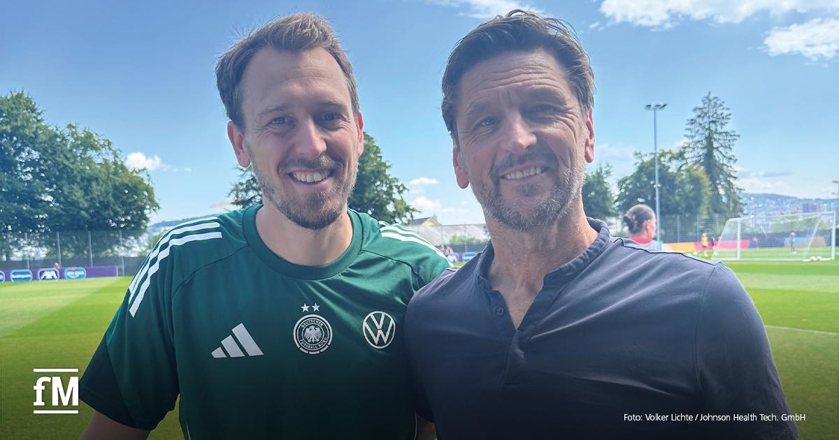 Zwei Männer (DFB-Frauen-Fitnesstrainer Julius Balsmeier und Volker Lichte, Matrix-Key-Account-Manager Performance and Sports) stehen auf einem Fußballfeld und lächeln in die Kamera.