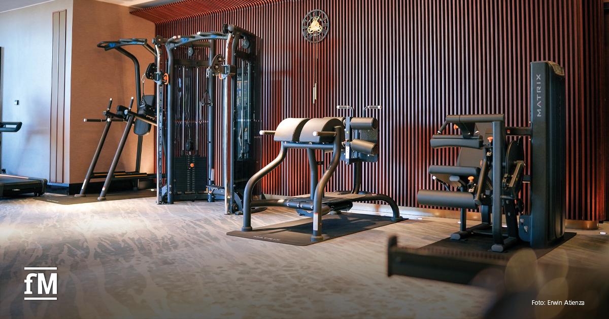 Fitnessraum mit mehreren Matrix-Trainingsgeräten vor Holzlamellenwand.