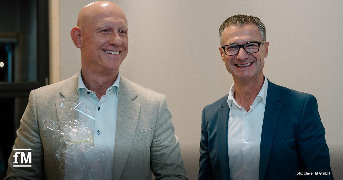 Zwei Männer in Anzügen lächeln bei einer Veranstaltung