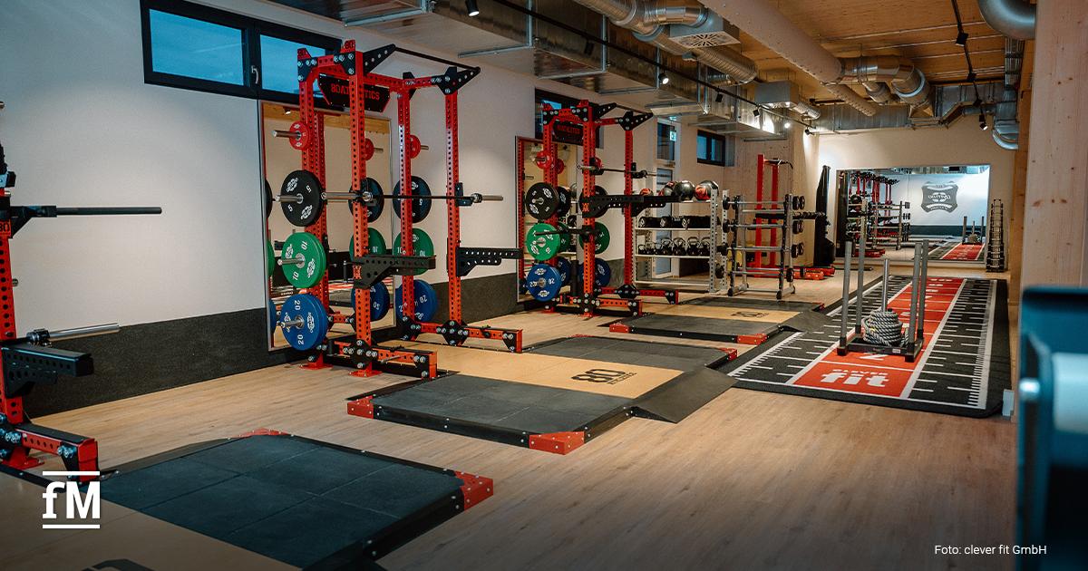 Trainingsbereich mit Hantelständern, Gewichtsscheiben und Geräten in modernem Holz- und Stahlambiente.