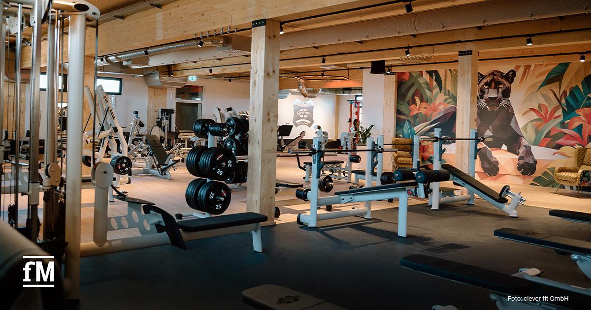 Große Trainingsfläche mit Geräten, Hanteln und Wandmalerei einer Raubkatze.