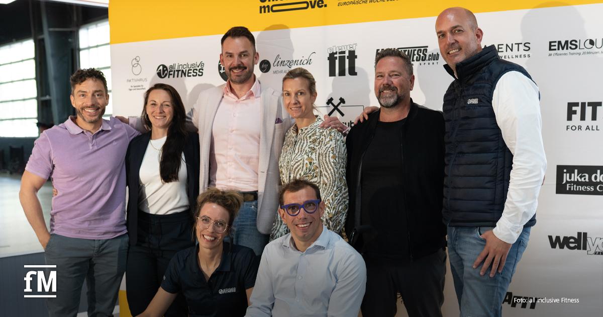 #BEACTIVE und 'United let's move.' Acht Personen posieren vor einer Pressewand mit Logos von Fitnessunternehmen für ein Gruppenfoto.