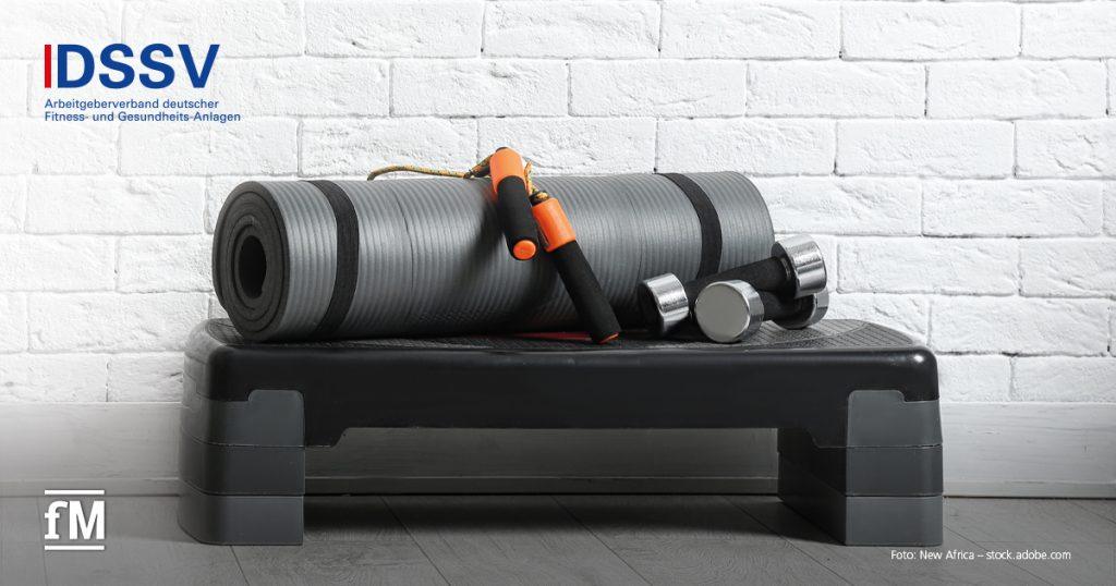 Graue Trainingsmatte, Kurzhanteln und Springseil auf einem Steppbrett, vor weißer Ziegelwand, links oben DSSV-Logo.