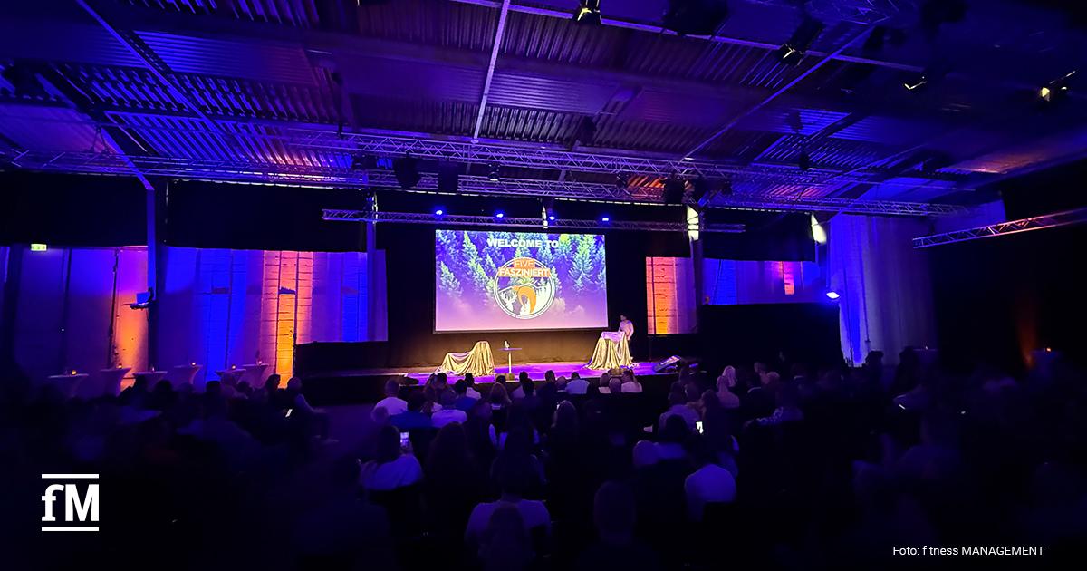 Blick in die stimmungsvoll beleuchtete Eventhalle mit großer Bühne und Publikum.