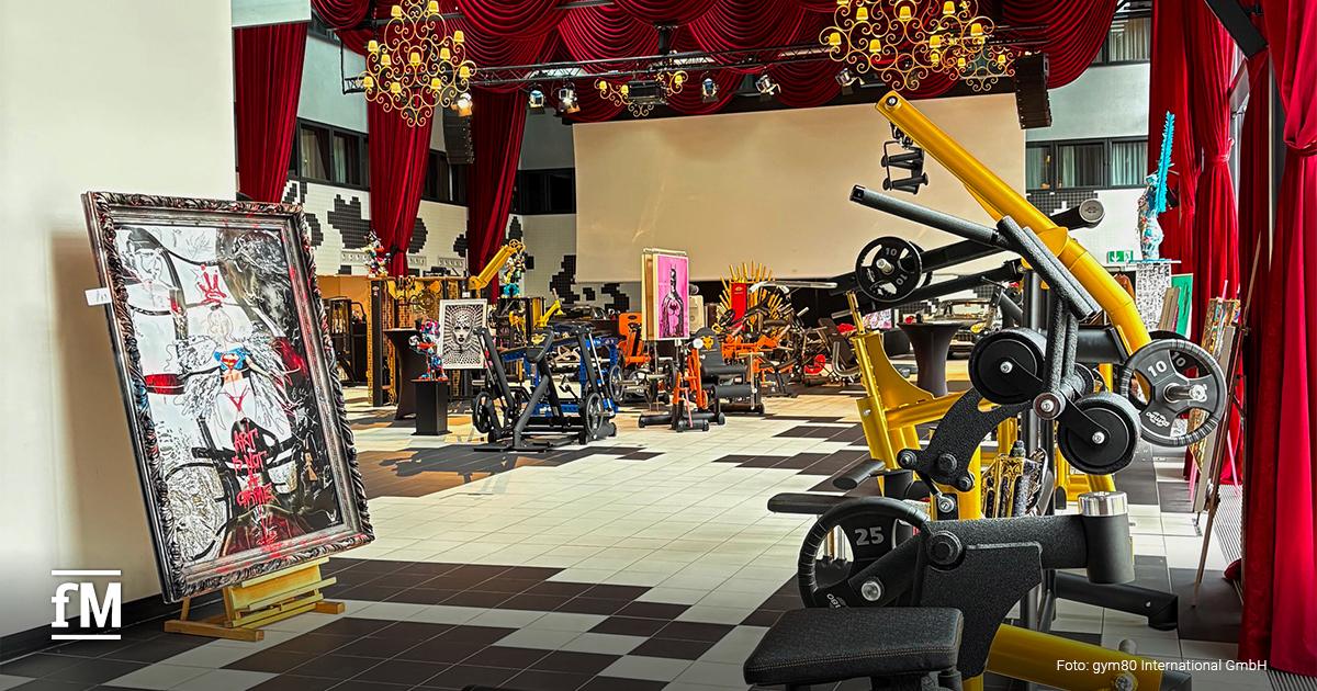 Verschiedene Fitnessgeräte und Kunstwerke stehen in einer stilvoll beleuchteten Halle mit roten Vorhängen