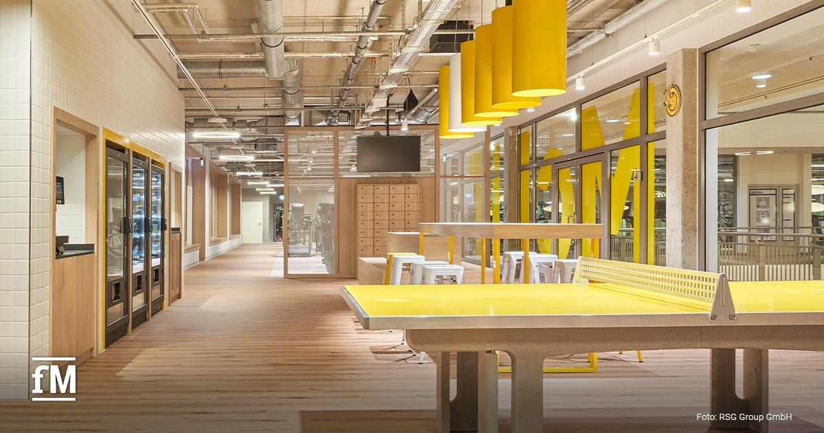 Lounge mit gelber Tischtennisplatte, Holzboden, Sitzmöbeln und Getränkeautomaten im McFIT Berlin-Prenzlauer Berg.