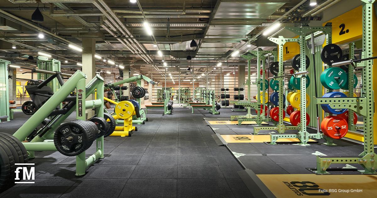 Kraftbereich mit mehreren Racks, Plattformen, farbigen Gewichtsscheiben und Maschinen im McFIT Berlin-Prenzlauer Berg.