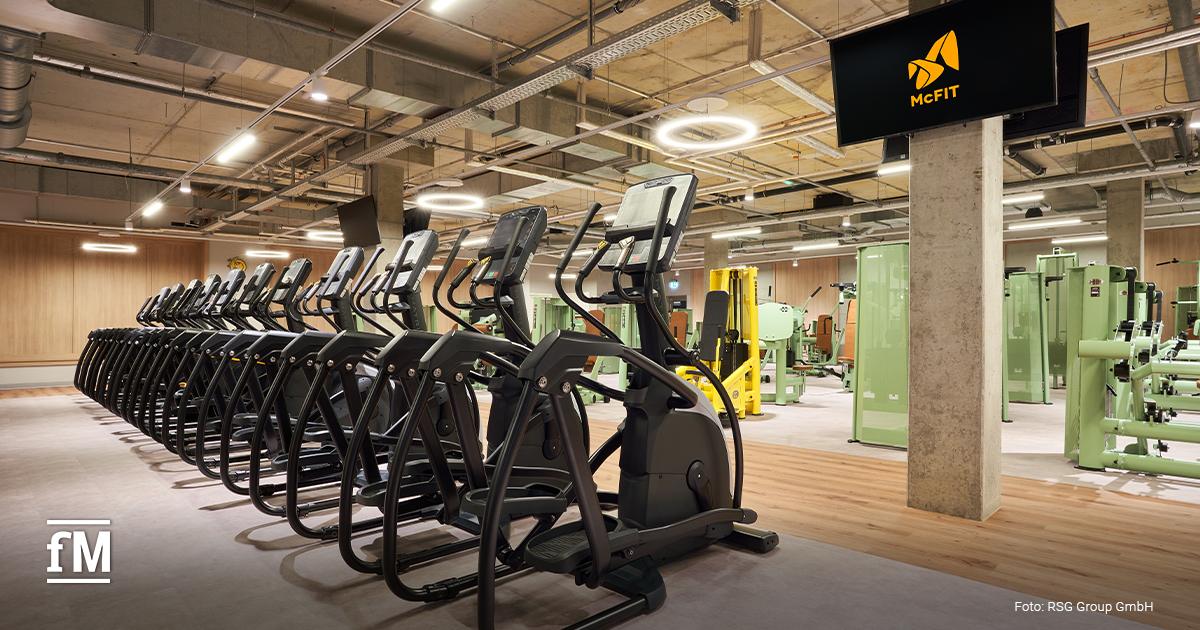 Reihe schwarzer Crosstrainer vor hellem Boden und grünen Kraftmaschinen im McFIT Berlin-Prenzlauer Berg