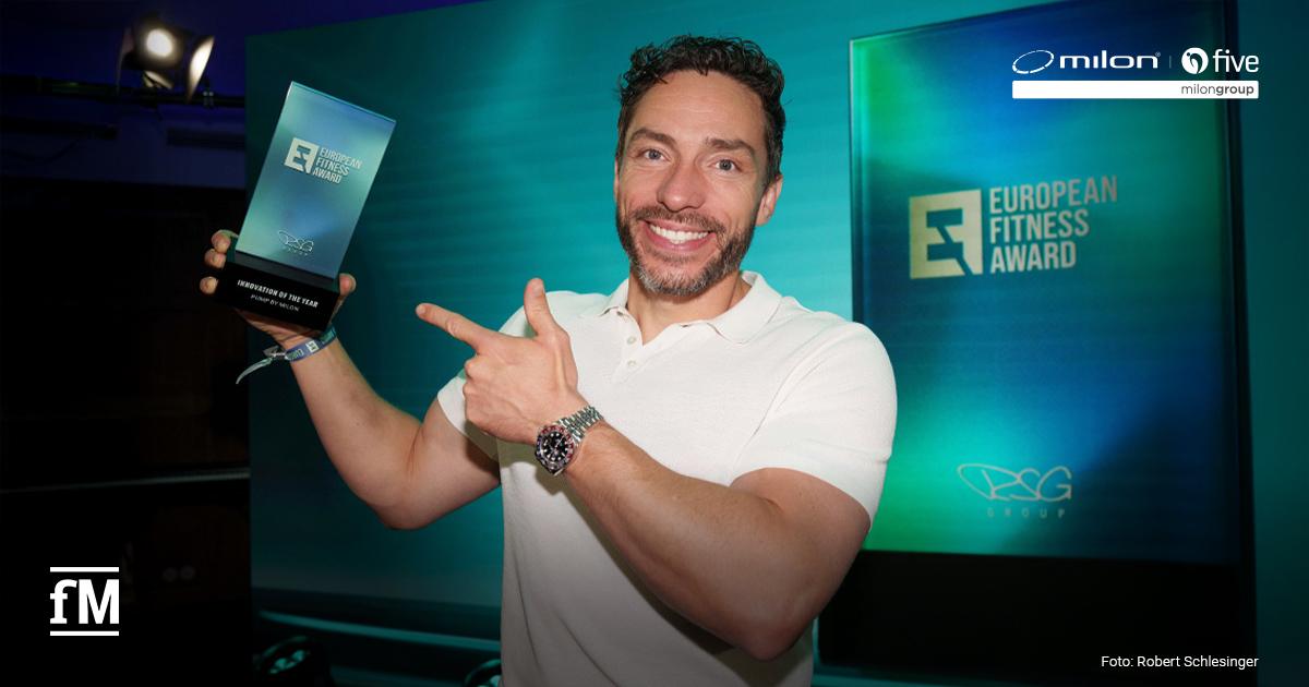 pump by milon European Fitness Award Mann im weißen Poloshirt hält einen European-Fitness-Award-Pokal vor grün-blauem Bühnenhintergrund in die Kamera.