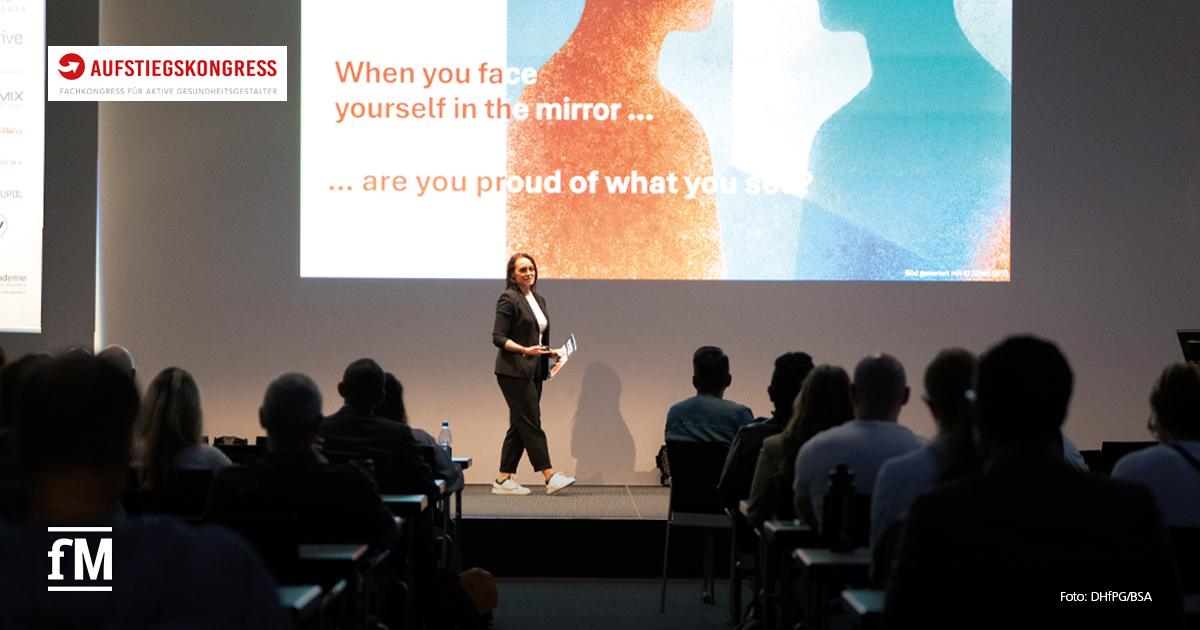 Referentin steht vor großer Leinwand mit Spiegelmotiv und englischem Zitat, Publikum sitzt im abgedunkelten Vortragssaal.