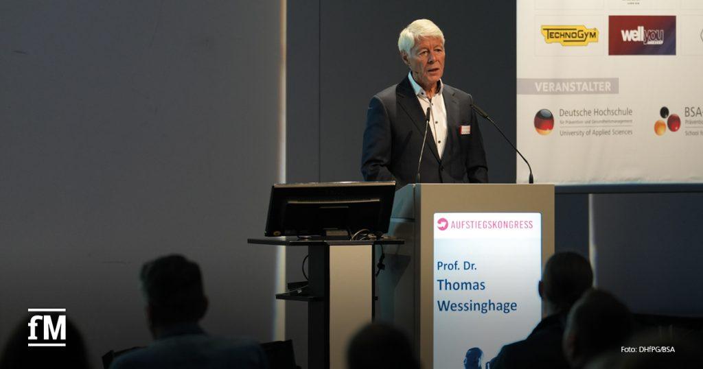 Älterer Mann im Anzug spricht am Rednerpult mit Aufstiegskongress-Logo, neben ihm Leinwand mit Sponsorenlogos.