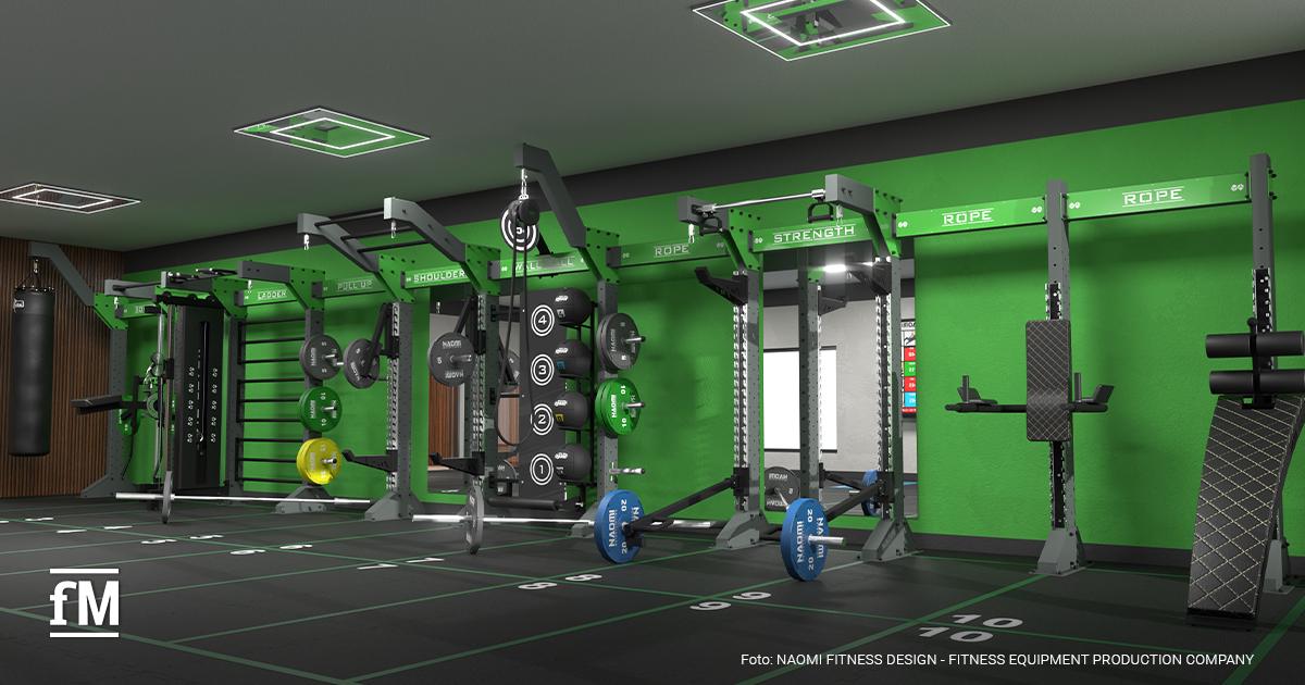 Leerer funktioneller Trainingsbereich mit grünen Rigs, Hantelscheiben und markiertem Boden in einem Fitnessstudio.