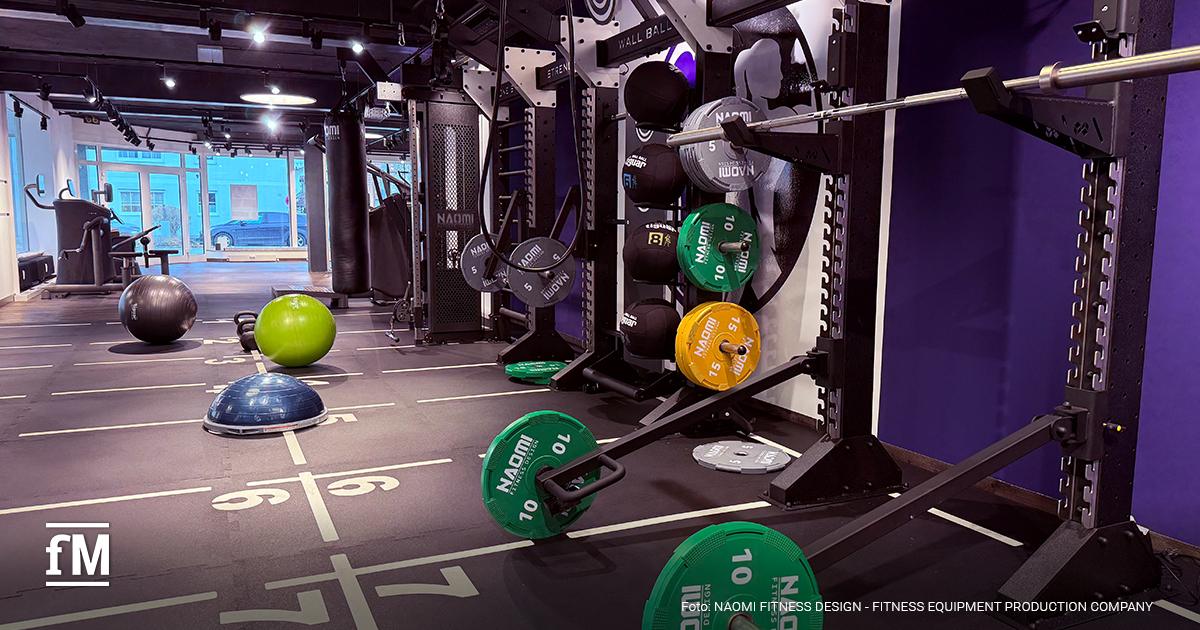 Funktionelle Trainingsfläche mit Rig, Hantelscheiben, Gymnastikbällen und Linien mit Zahlen (5, 6, 7 im Vordergrund) in einem Fitnessstudio.