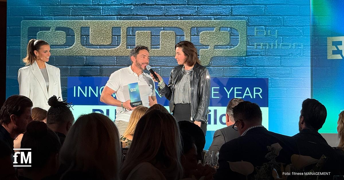 Drei Personen auf einer Bühne vor großer LED-Wand mit 'pump by milon'-Logo, eine Person hält ein Mikrofon und ein Award in der Hand.