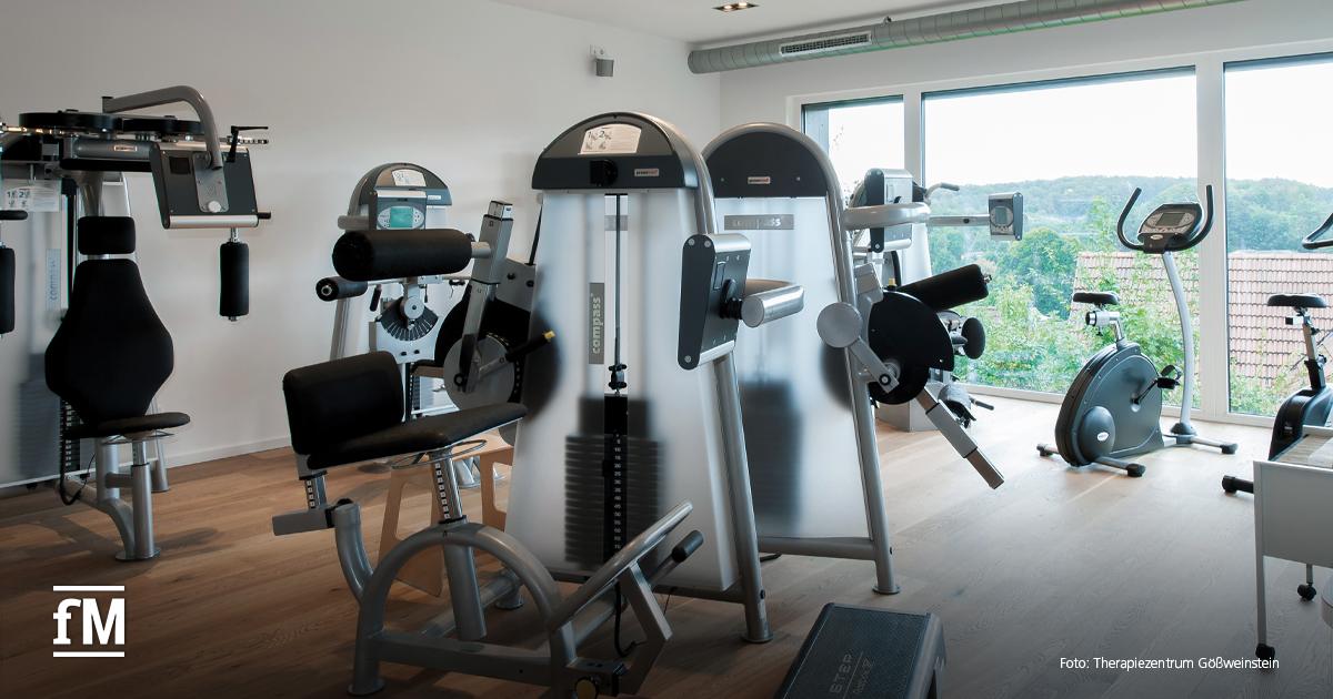 Mehrere silberfarbene Trainingsgeräte stehen in einem hellen Raum mit Holzfußboden und großen Fenstern.