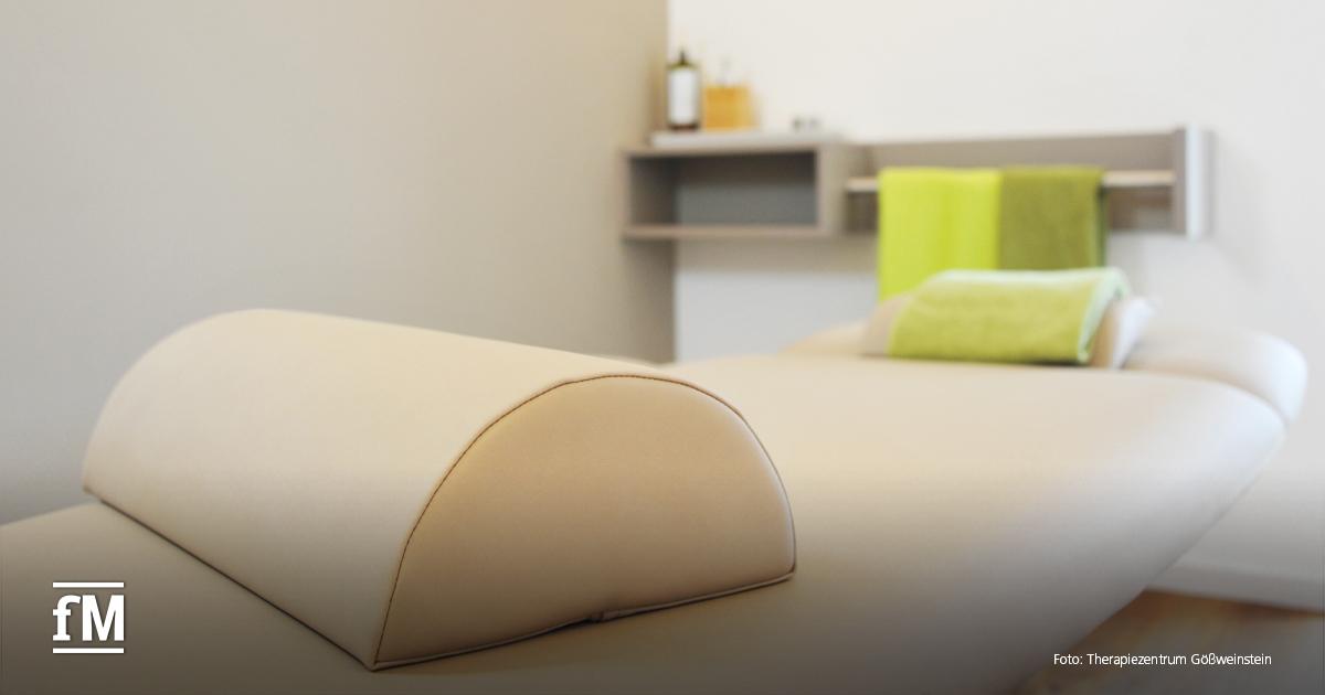 Heller Raum mit beiger Therapieliege, Handtüchern und Ablage an der Wand.