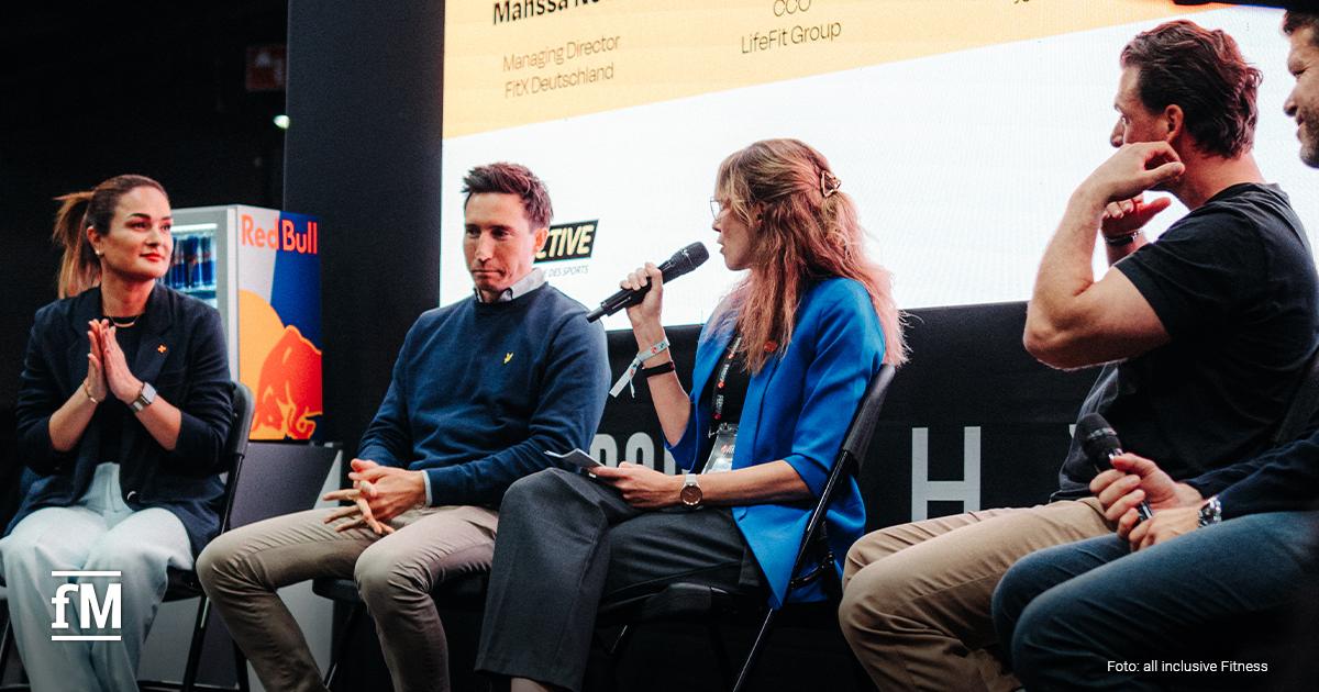 Fünf Personen sitzen auf einer Bühne, eine Frau mit Mikrofon moderiert das Gespräch.