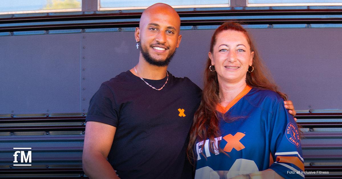 Ein Mann und eine Frau in FitX-Shirts lächeln in die Kamera und stehen Arm in Arm.