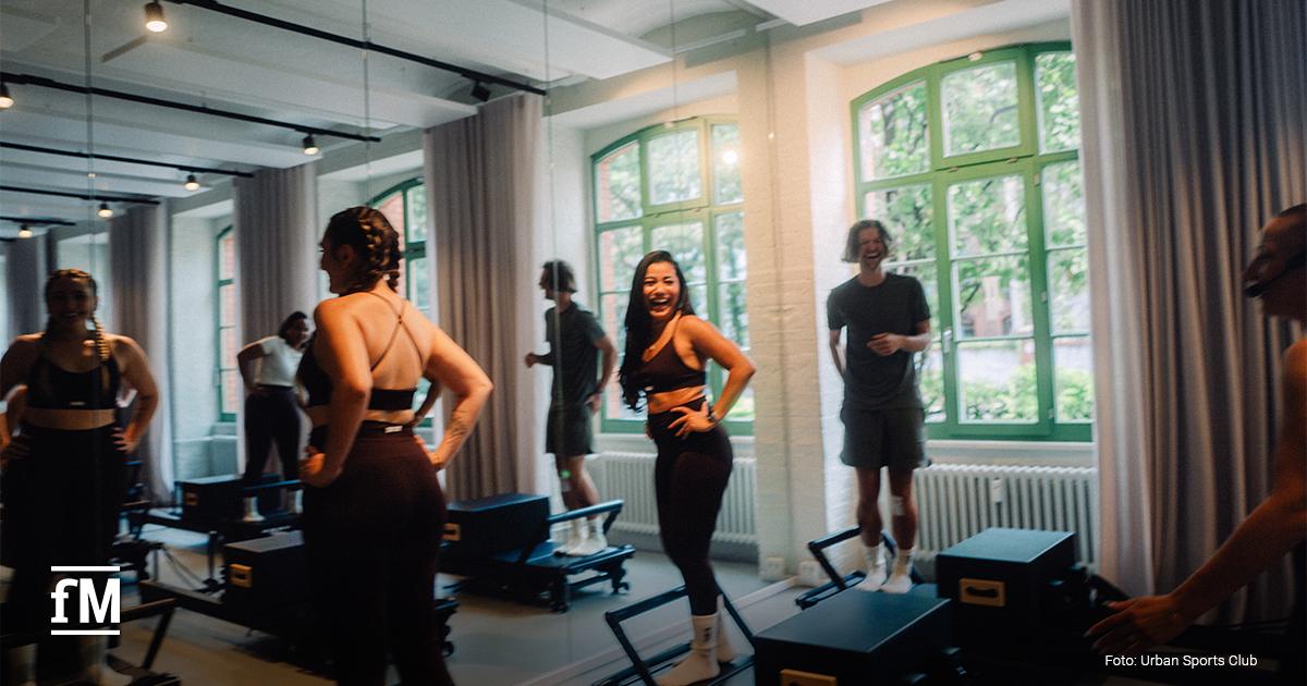 Trainerin demonstriert Pilates-Übung in einem hellen Boutique-Studio mit Spiegelwand