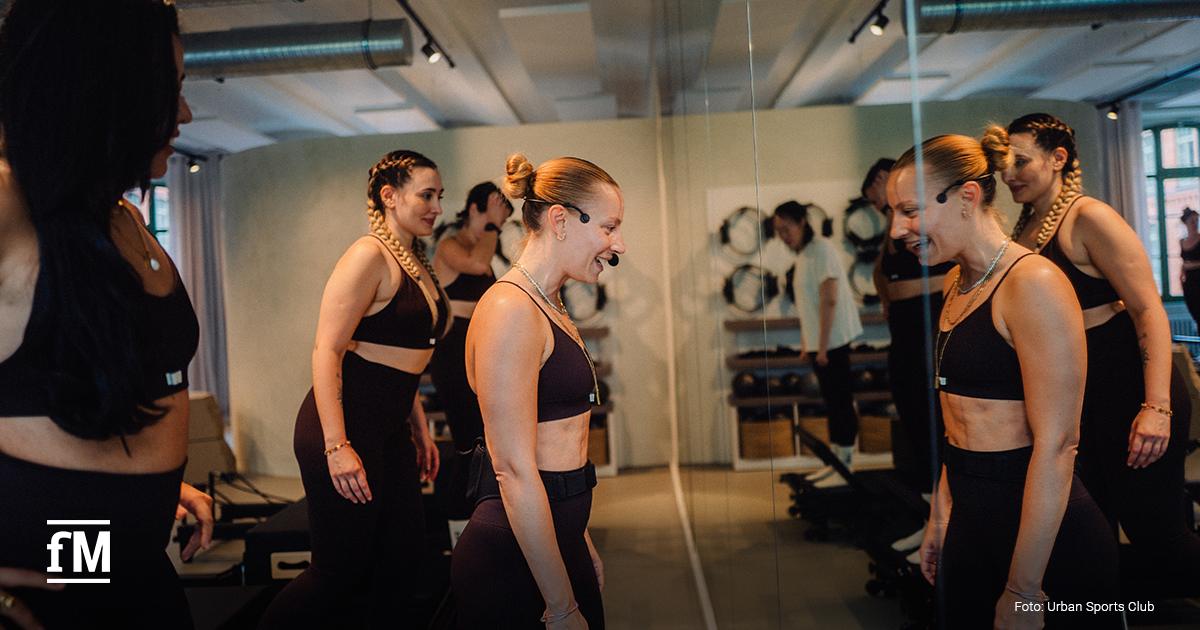 Trainerin demonstriert Pilates-Übung in einem hellen Boutique-Studio mit Spiegelwand